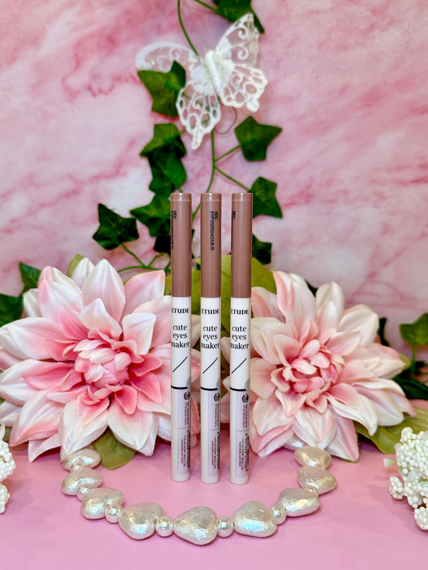 three lip glosses sitting on top of a pink table