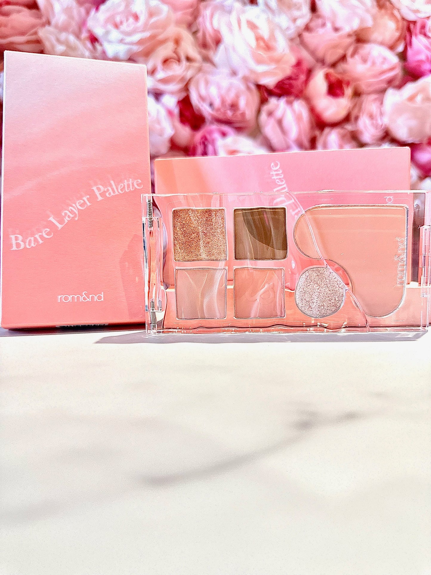 The rom&nd Bare Layer Mood Palette elegantly displayed with a charming pink background, showcasing its gorgeous shades for versatile looks.