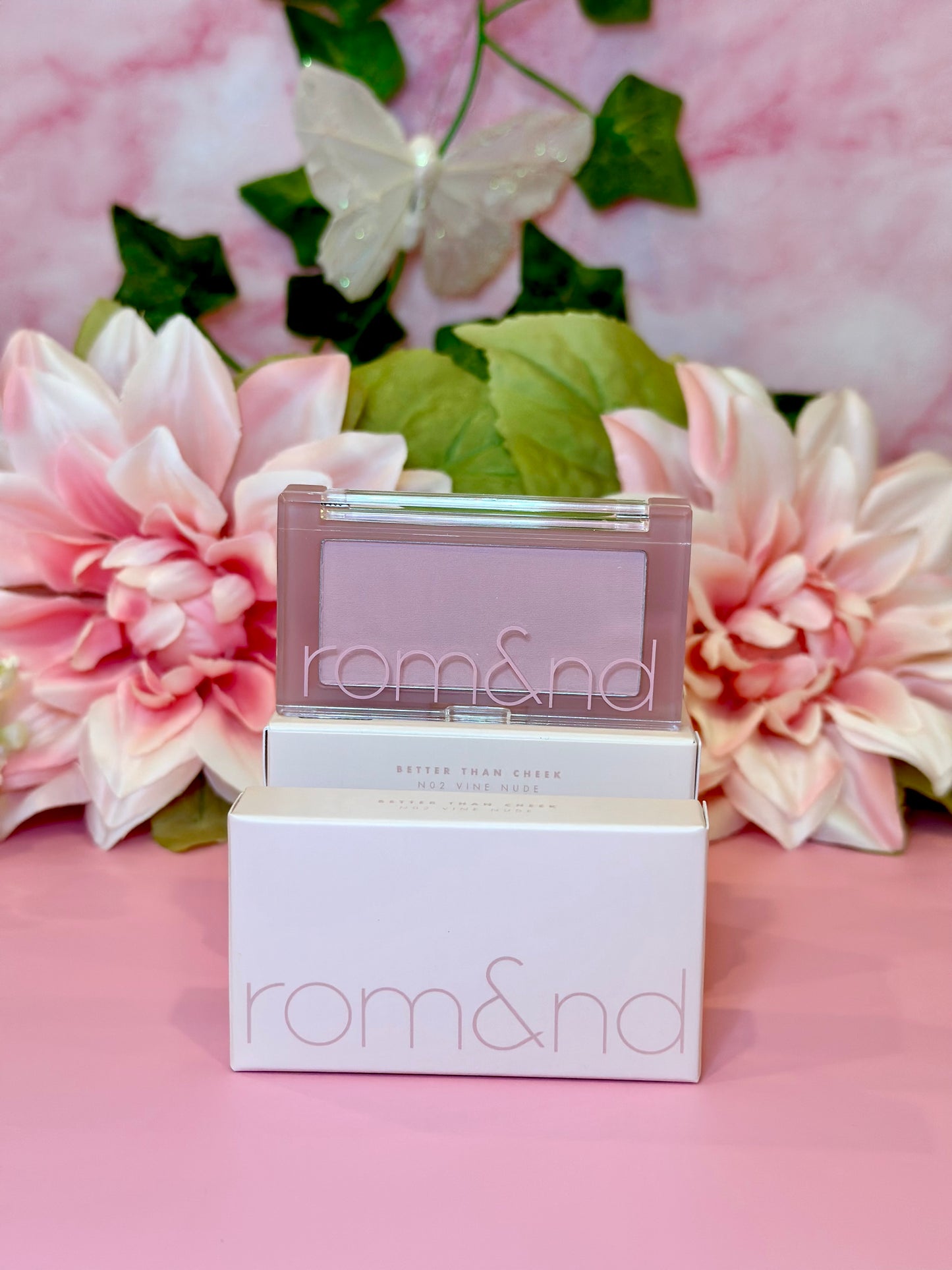 A charming display of rom&nd Better Than Cheek blush in N02 Vine Nude with blooming floral arrangements, merging elegance and beauty for a delightful blush experience.