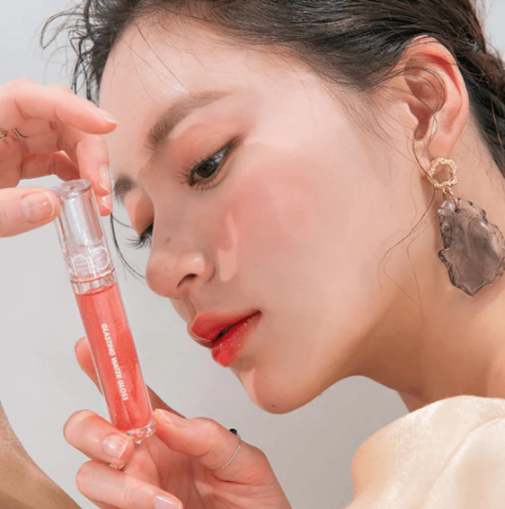 A beautiful moment with a model applying rom&nd Glasting Water Gloss, showcasing a luscious shade with shiny, plump lips.
