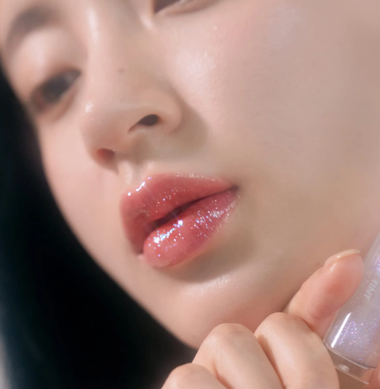 Glistening lips featuring rom&nd Glasting Water Gloss in Sanho Crush shade, emphasizing the pink and gold speckled gloss.