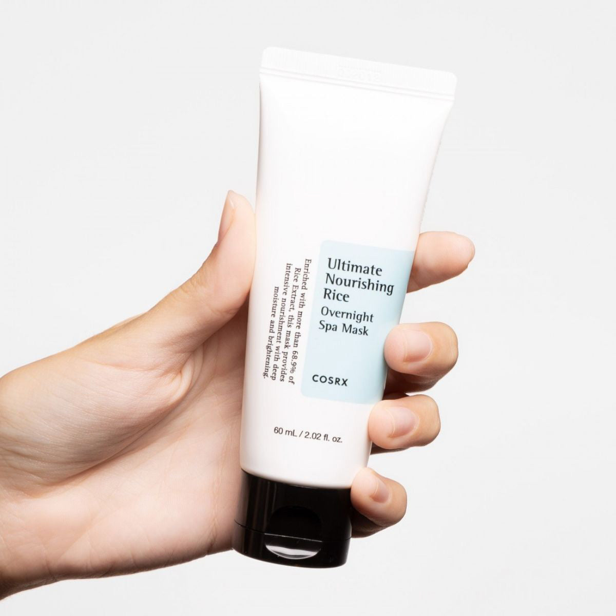 a hand holding a tube of white cream