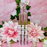 three lip glosses sitting on top of a pink table