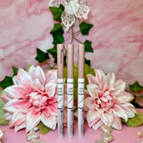 three lip glosses sitting on top of a pink table