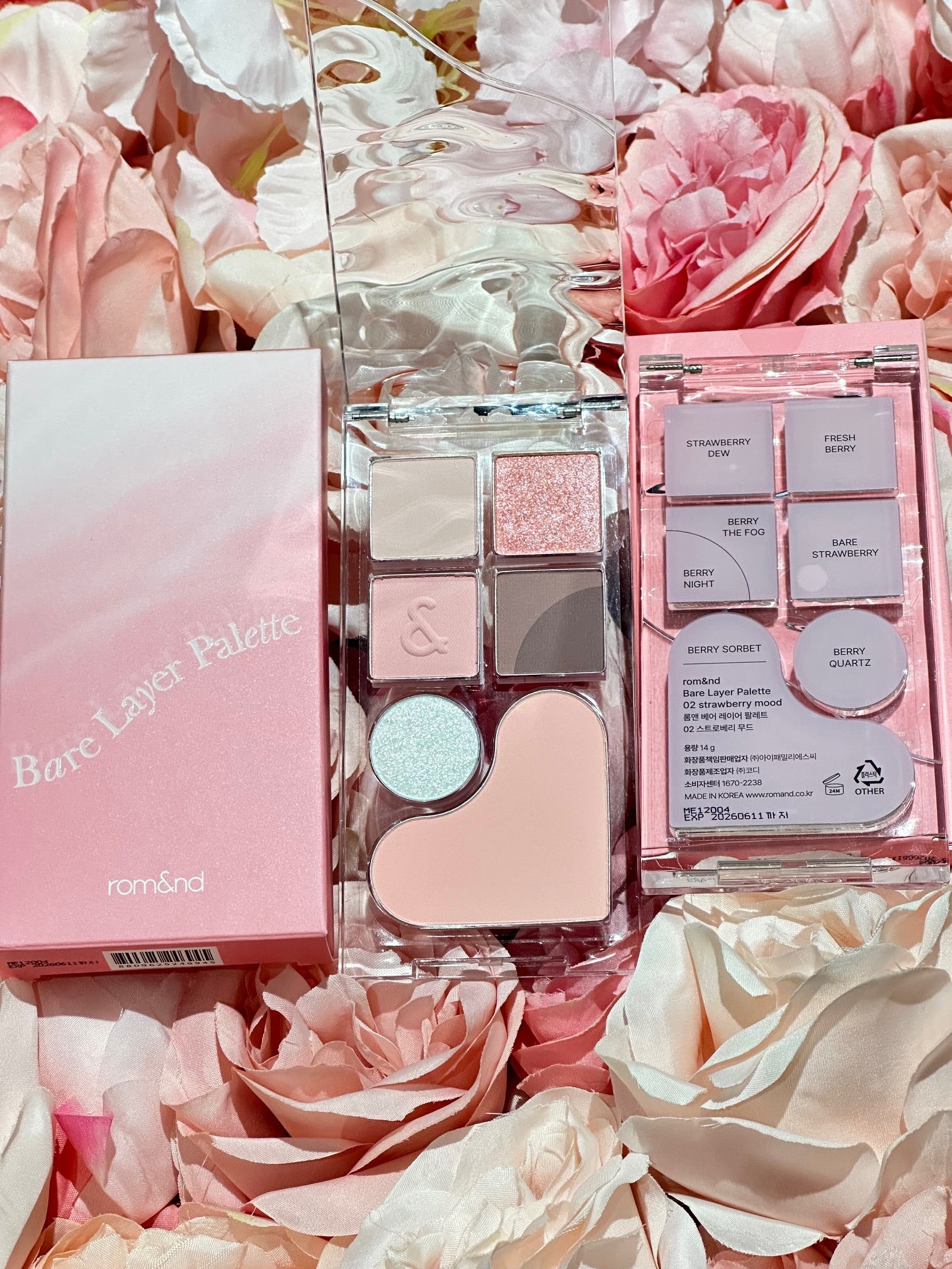 The rom&nd Bare Layer Mood Palette nestled among soft pink roses, highlighting the aesthetic charm of its Strawberry Mood design.
