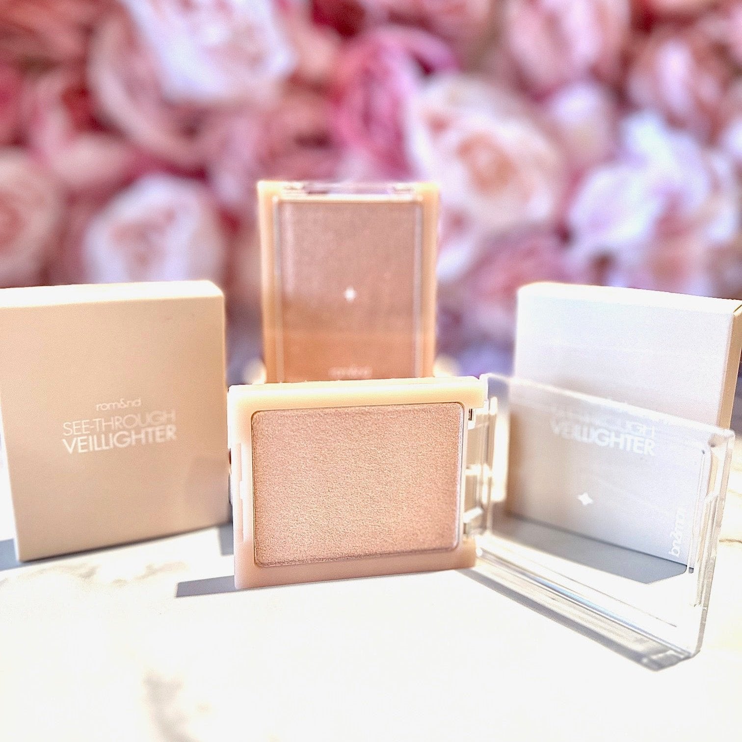rom&nd See-Through Veil Lighter with an open compact, displaying the shimmering highlighter alongside its stylish packaging.