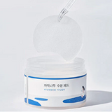 Round Lab Birch Juice Moisturizing Pad jar being opened to reveal its inner lid and pad, emphasizing convenience and freshness of the product for skin hydration.