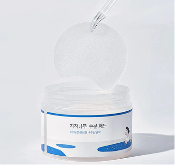 Round Lab Birch Juice Moisturizing Pad jar being opened to reveal its inner lid and pad, emphasizing convenience and freshness of the product for skin hydration.
