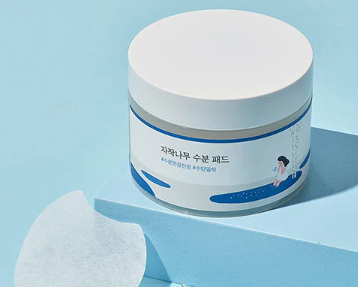 Stylish presentation of Round Lab Birch Juice Moisturizing Pad on a bright background, showcasing the jar and a single pad, illustrating its refreshing and moisturizing properties.