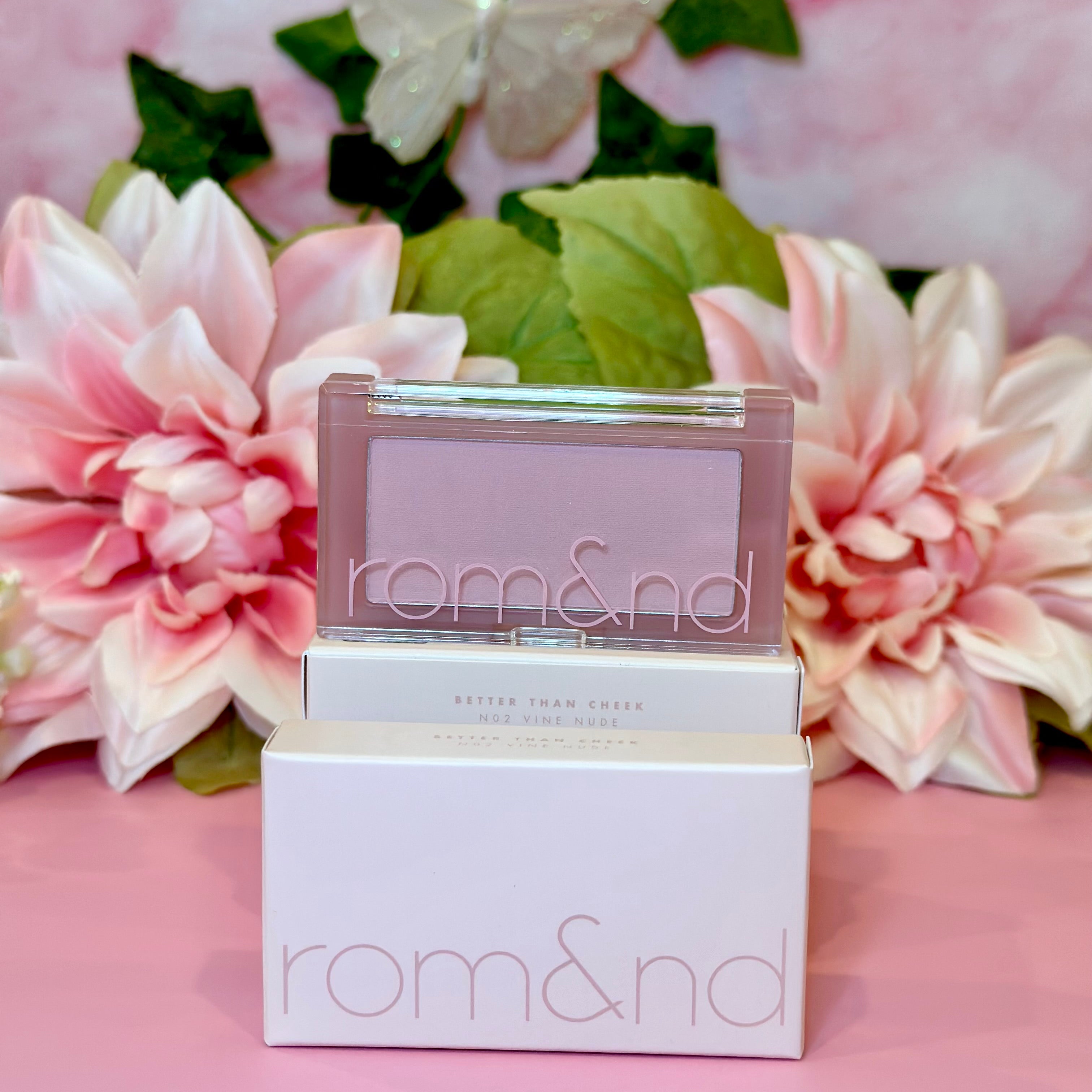 A charming display of rom&nd Better Than Cheek blush in N02 Vine Nude with blooming floral arrangements, merging elegance and beauty for a delightful blush experience.
