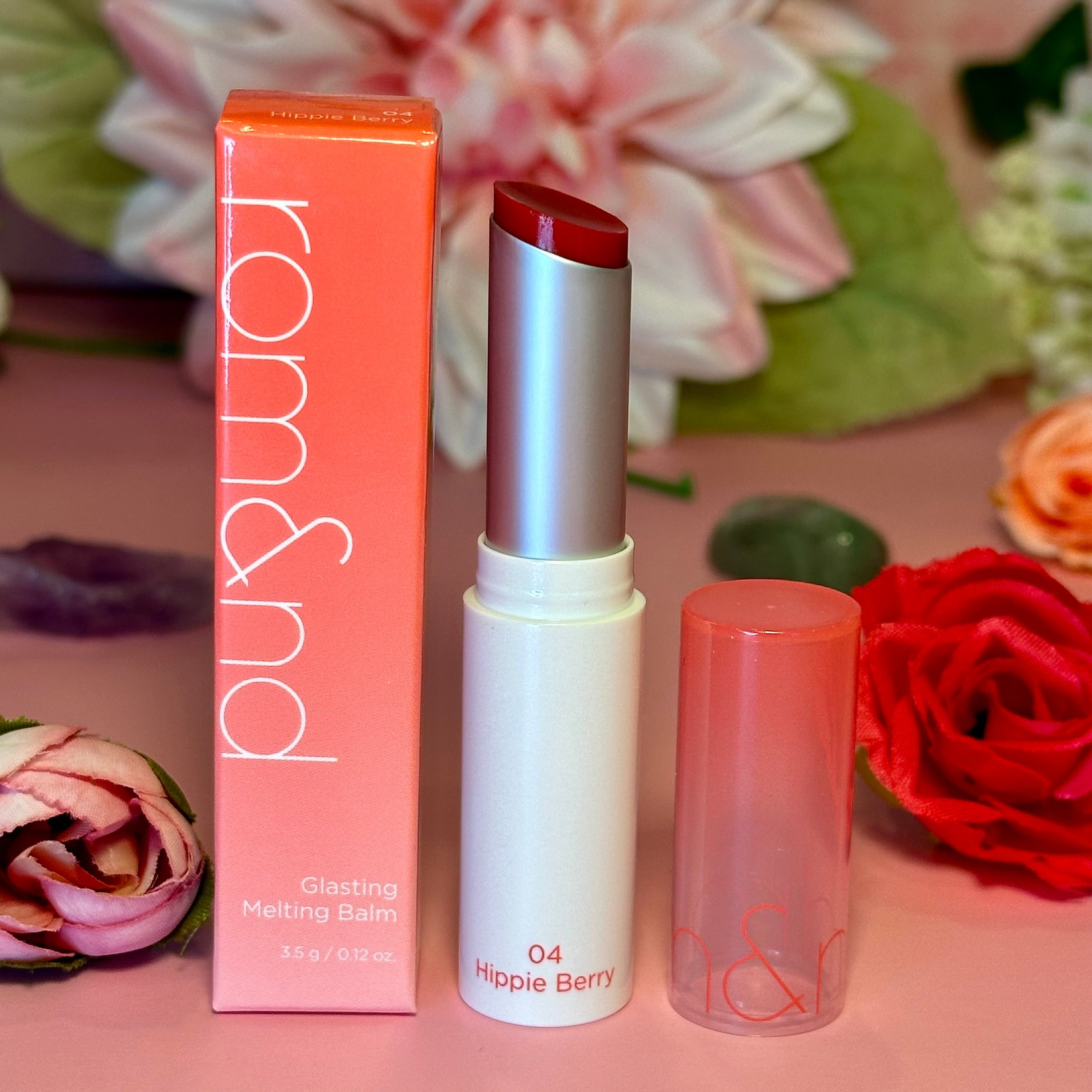 rom&nd Glasting Melting Balm in the shade 04 Hippie Berry, displayed with the product box and pink florals for an elegant presentation.