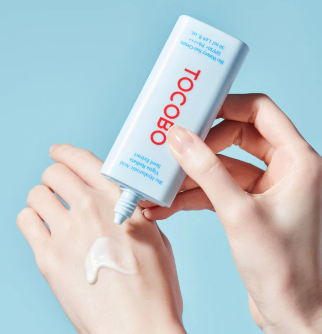 A hand applying Tocobo Bio Watery Sun Cream SPF50+ PA++++ on skin, demonstrating its light and moisturizing formula suitable for sensitive skin.