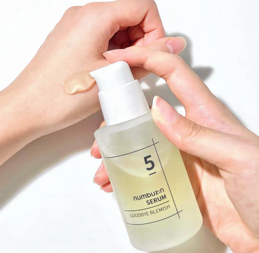 Close-up shot of hands applying Numbuzin No.5 Goodbye Blemish Serum, illustrating its smooth texture and user-friendly pump.